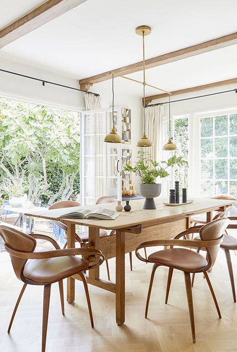 an airy neutral dining room with a stained table and chairs, greenery, a gold chandelier and a lovely garden view