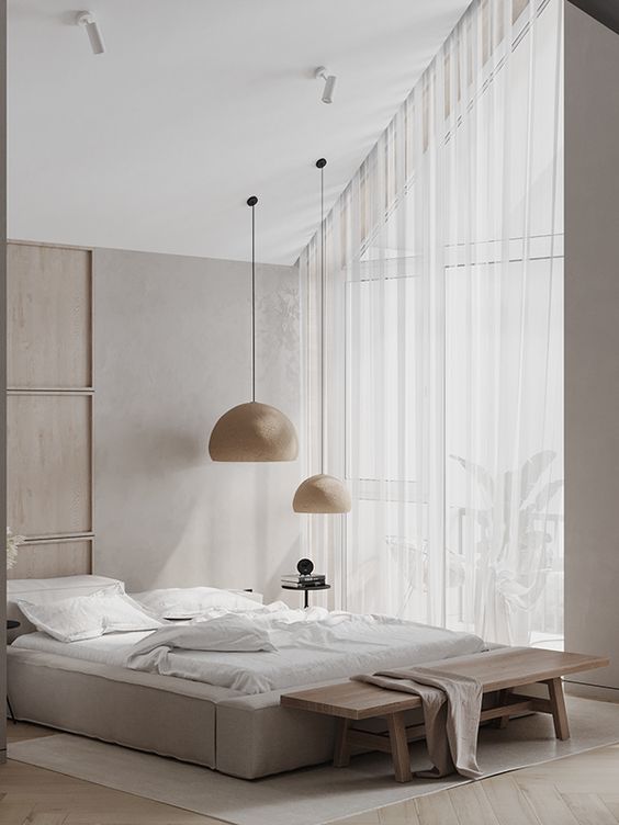an attic contemporary to minimalist neutral bedroom with a low upholstered bed, a duo of pendant lamps, a bench and a glazed wall