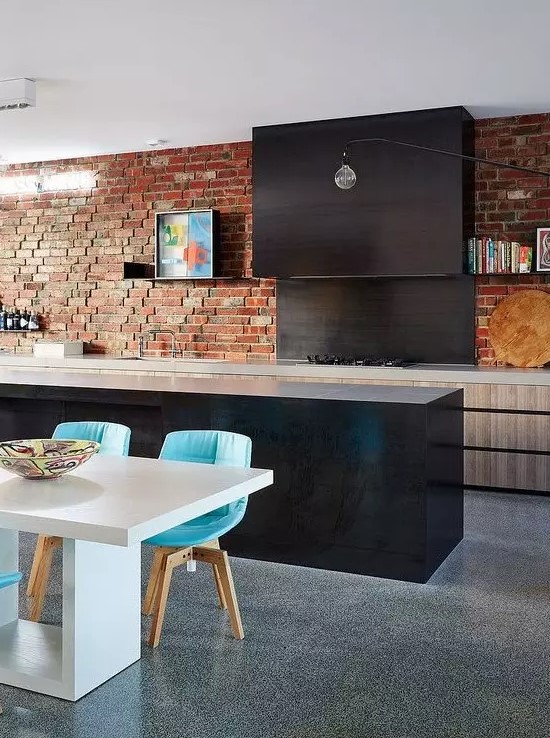 an eclectic kitchen with sleek light and dark cabinets, a red brick wall and bright turquoise chairs