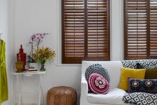 an eclectic white living room with stained shutters, bright textiles, blooms and vases is a bold and cool space