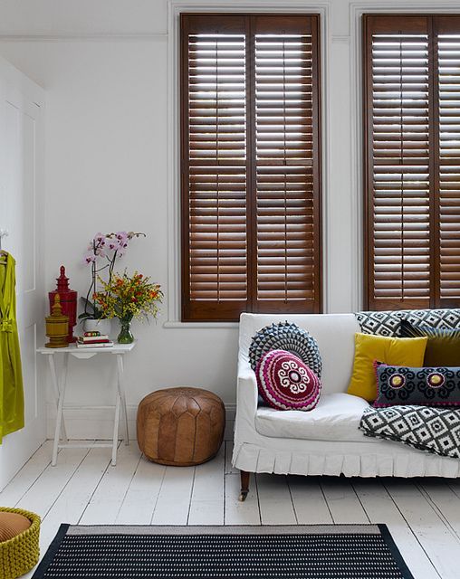 an eclectic white living room with stained shutters, bright textiles, blooms and vases is a bold and cool space