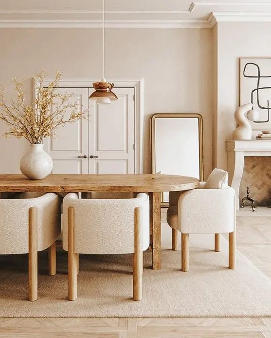 an elegant and chic neutral dining room with a stained table, neutral chairs, a fireplace clad with brick, a floor mirror and a very stylish pendant lamp