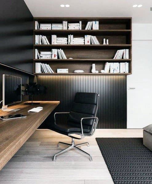 an elegant contemporary home office with black wooden slat paneling, a floating desk, a bookshelf on the wall, built in lights and a black chair