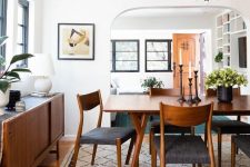an elegant mid-century modern dining room with a stained table, chairs and a credenza, potted greenery and a chic chandelier