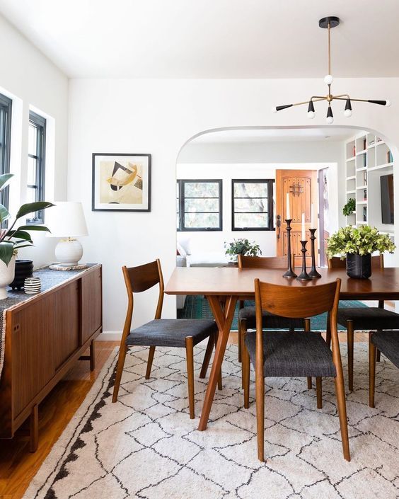 an elegant mid century modern dining room with a stained table, chairs and a credenza, potted greenery and a chic chandelier