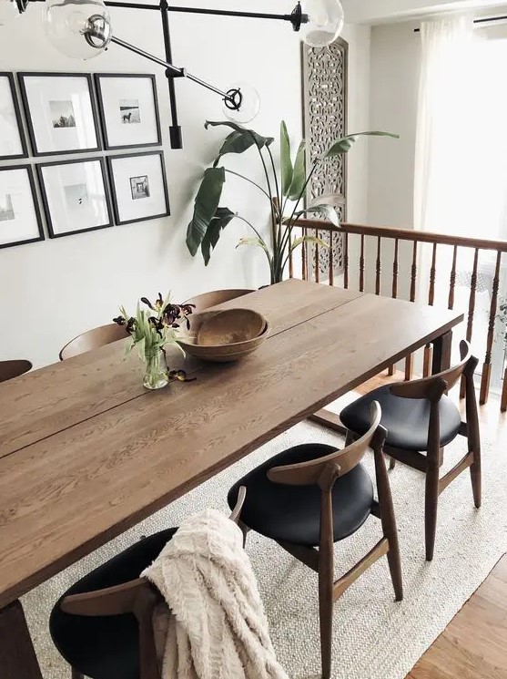 an elegant mid-century modern dining space with a stained table and black chairs, a gallery wall and a chic chandelier plus greenery here and there