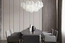 an exquisite greige dining room with paneled walls, stained wood, a black dining table, grey chairs and a bubble pendant lamp