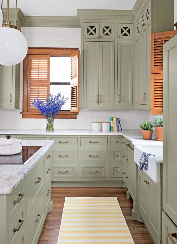 an olive green kitchen with shaker style cabinets, white countertops, orange shutters for a bright touch of color