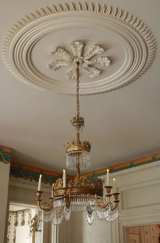 an oversized refined off-white ceiling medallion that matches the color of the ceiling and a whimsical crystal and gold chandelier with candles