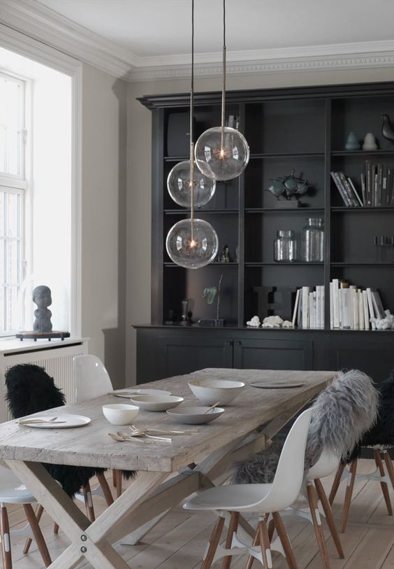 monochromatic Scandinavian dining space with a trestle table, white chairs, a cluster of pendant lamps and a black buffet