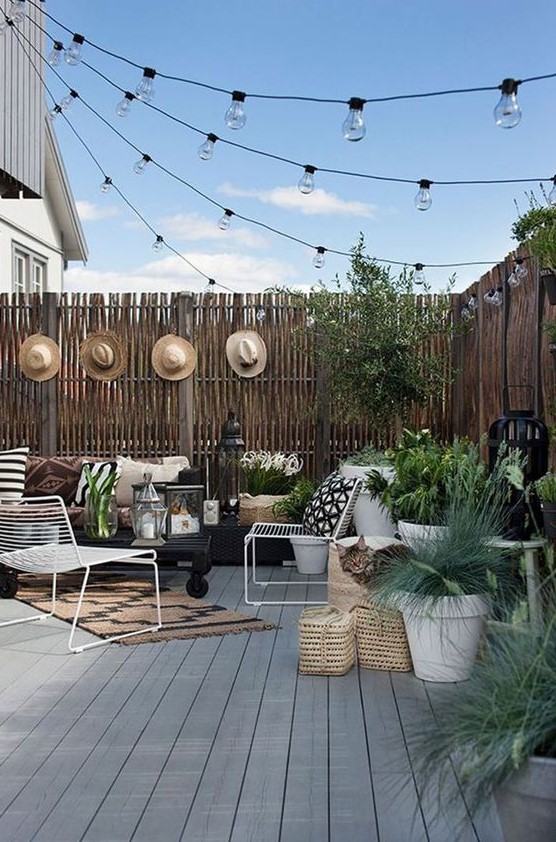 a backyard deck styled with string lights over the space and some candle lanterns on the deck is very welcoming and chic