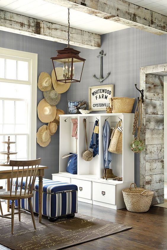 a beach cottage space with grey walls, a hat display on the wall, a white storage unit, stained furnture and a striped pouf