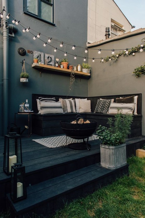 a Nordic backyard space with graphic pillows, lots of potted plants and string lights over the space