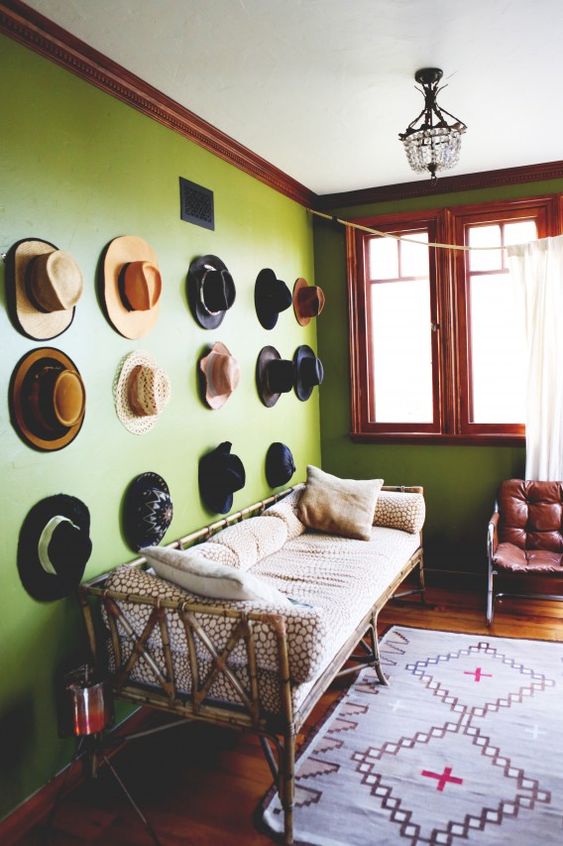 a hat gallery wall over a bamboo daybed, a burgundy leather chair and a printed rug are amazing for a bold space
