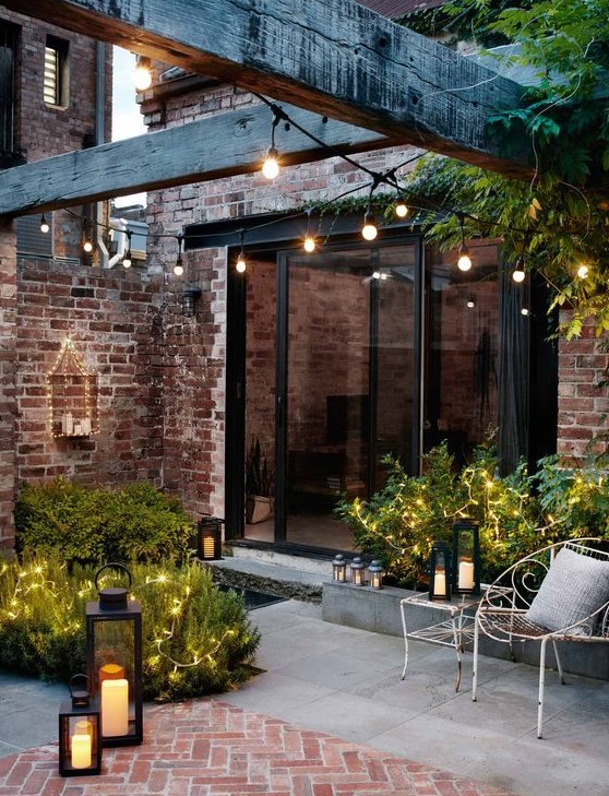 a refined backyard with fairy lights on plants, string lights over the space and candle lanterns all around