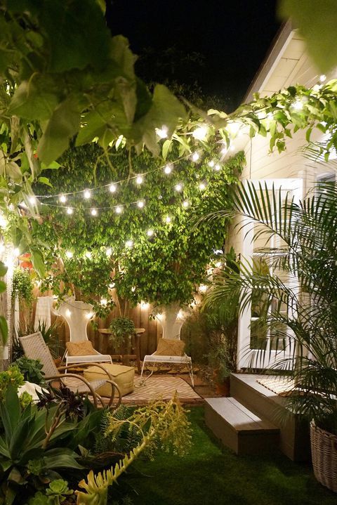 a small and pretty backyard with cool chairs and a rocker, with greenery and string lights over the space