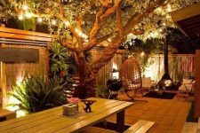 13 a stylish and cozy backyard with strign lights on the branches and built-in lights looks very welcoming