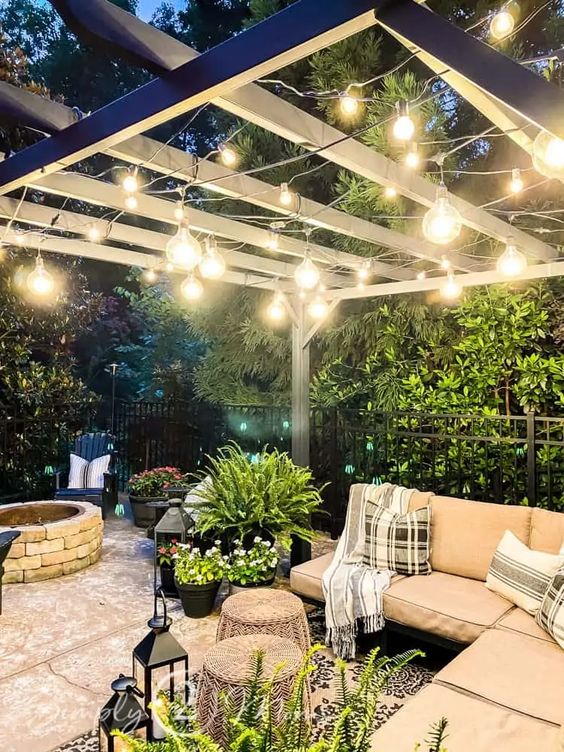 a stylish neutral outdoor space with a corner sofa, some stools, greenery, lanterns and string lights over the space