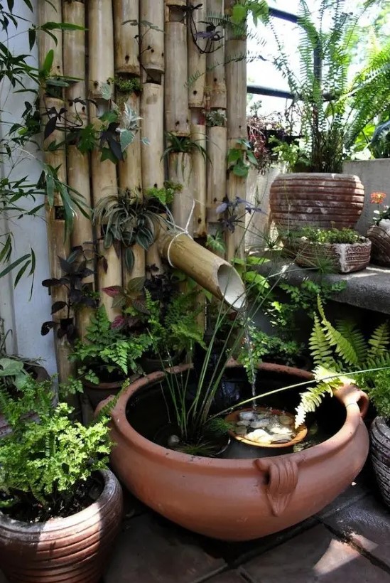 a Japanese-inspired bamboo wall with greenery, a porcelain bowl and pebbles and greenery plus a bamboo fountain
