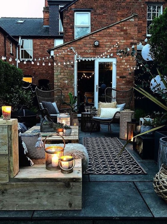 a welcoming backyard with pallet and rattan furniture, with printed textiles, candle lanterns and string lights over the space