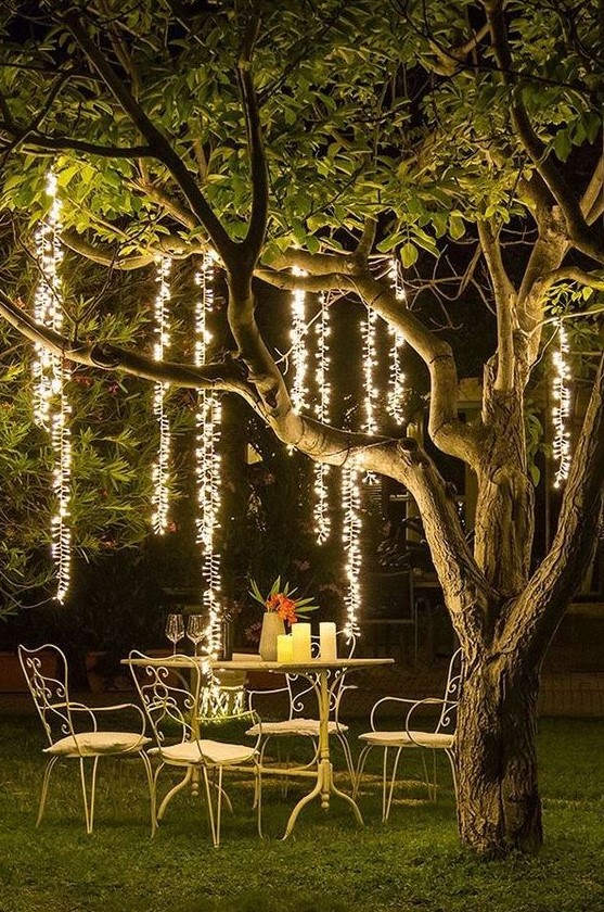an outdoor dining space with refined metal furniture, candles on the table and hanging lights over the space