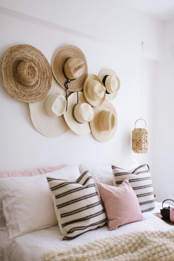 a pretty boho bedroom with a neutral bed and printed bedding, a hat gallery wall instead of a headboard, a woven pendant lamp