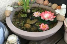 25 a small container pond with water plants and faux blooms, with rocks and decor around can be placed even in a balcony