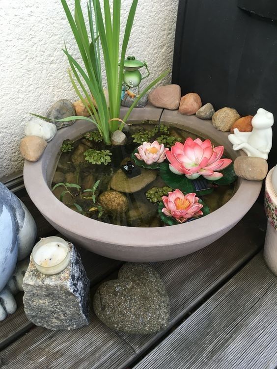 a small container pond with water plants and faux blooms, with rocks and decor around can be placed even in a balcony