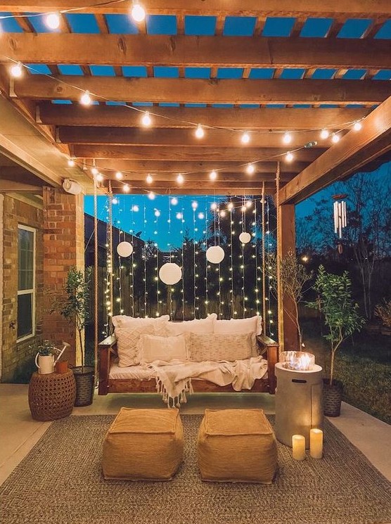 vertical and usual string lights plus paper lamps and candles and a modern fire pit is a stylish idea for a backyard