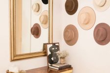 26 an elegant entryway with a chic stone slab console, a large mirror in a lovely frame and a gallery wall of hats that match in color