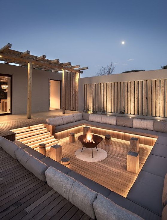 a refined contemporary backyard with built-in lights and a fire pit is a very welcoming and stylish idea