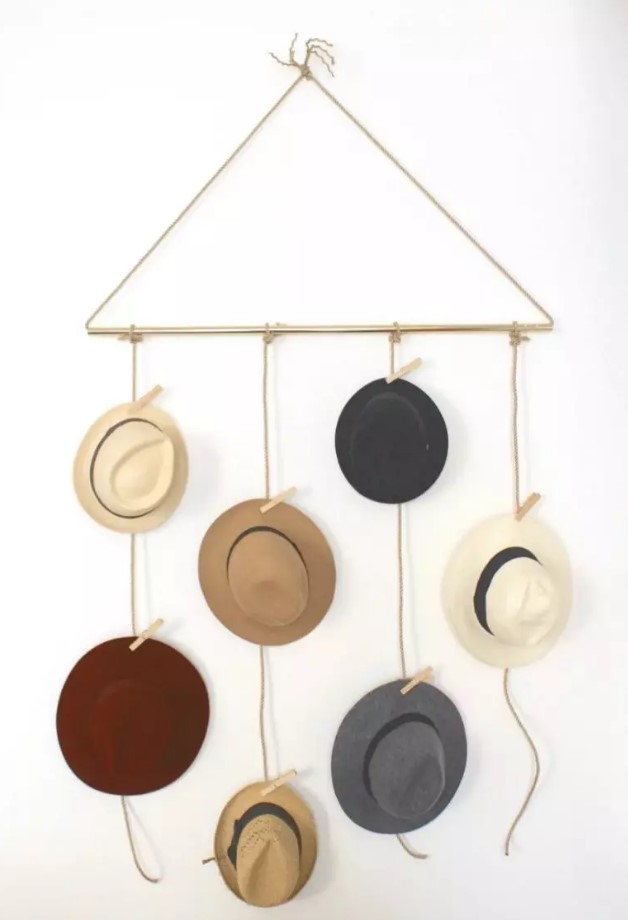 a pretty and simple hat holder of rope and a gold tube, with hats hanging on the rope and clothes pins is an easy piece that can be DIYed