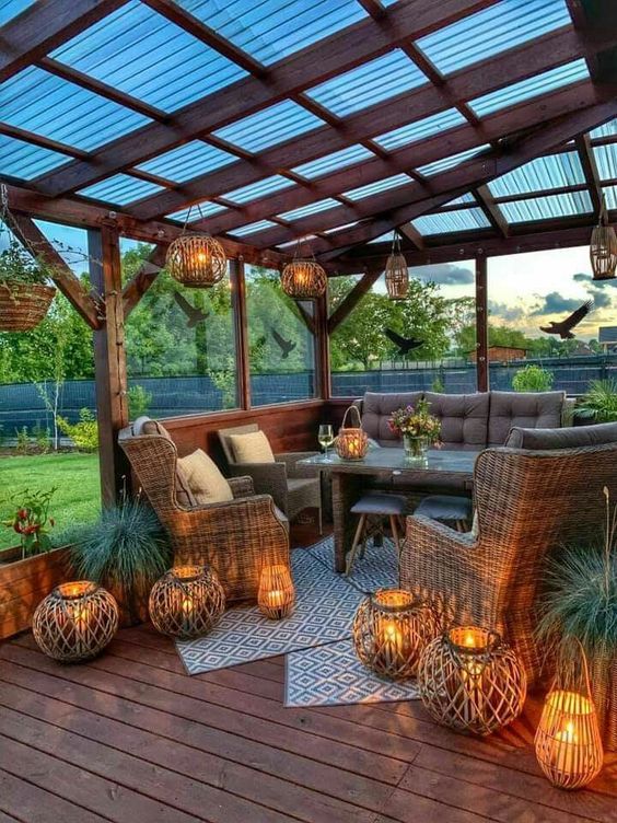 a terrace under a roof, with wicker and wooden furniture, greenery and lots of candles lanterns for lights