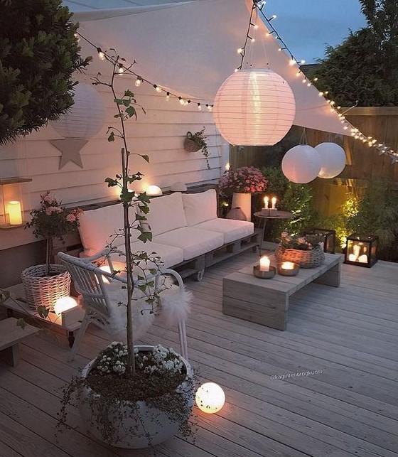 a welcoming deck with modern pallet and rattan furniture, candle lanterns, string lights and paper lamps over the space