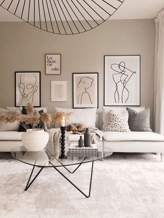 a Scandinavian greige living room with a white sofa, pillows, a gallery wall, a black chandelier and a glass table with decor