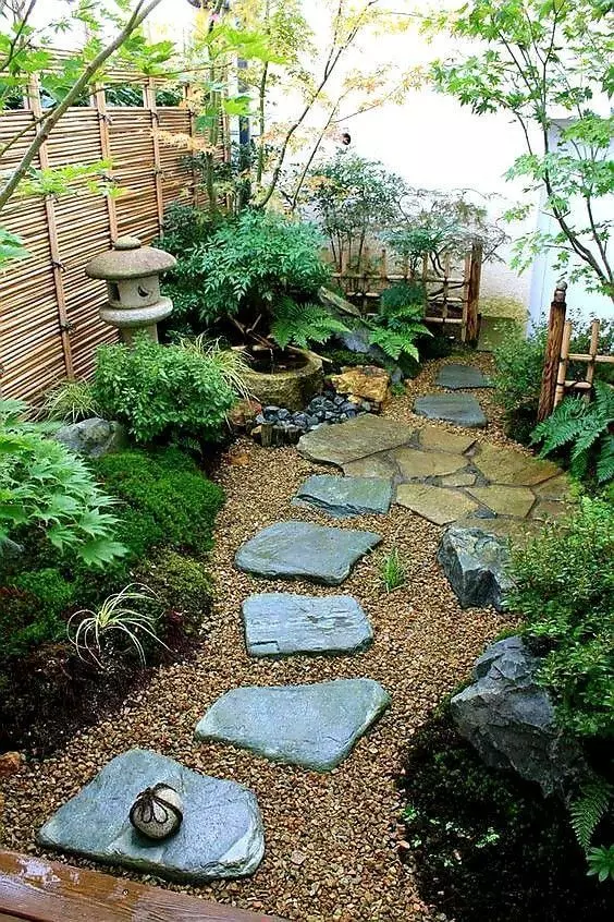a beautiful Japanese garden at the entrance,w ith rocks as steps, potted greenery, a stone lantern and some trees and leaves
