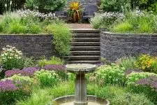 a beautiful and chic garden with lots of greenery and bold blooms, with a tiered fountain is a lovely space