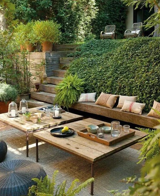 a beautiful and welcoming sunken terrace with greenery, built-in benches and low tables plus poufs is an amazing outdoor space