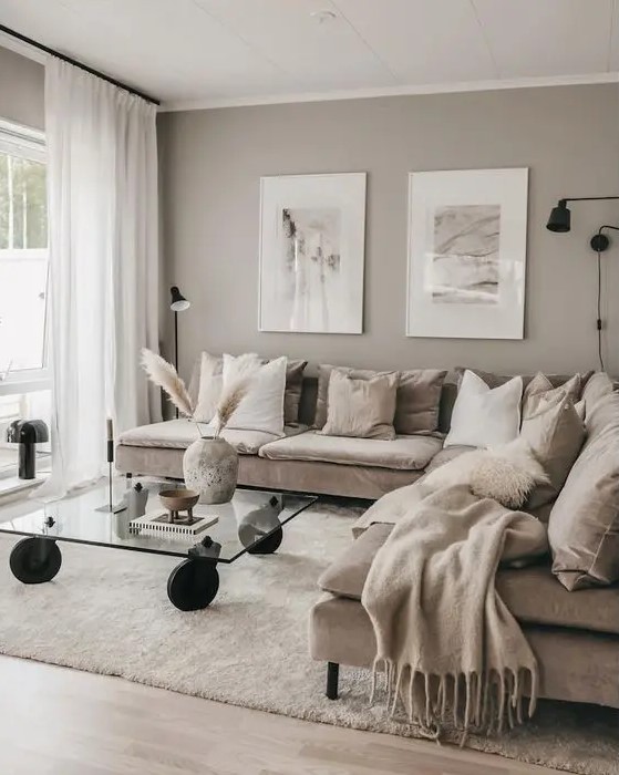 a beautiful greige living room with a cozy tan sectional, a glass table on casters, some pictures and a black sconce is a lovely idea