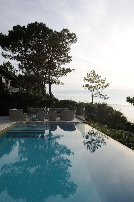 a beautiful infinity pool with steps and a neutral sitting zone plus greenery, trees and a fantastic sea view