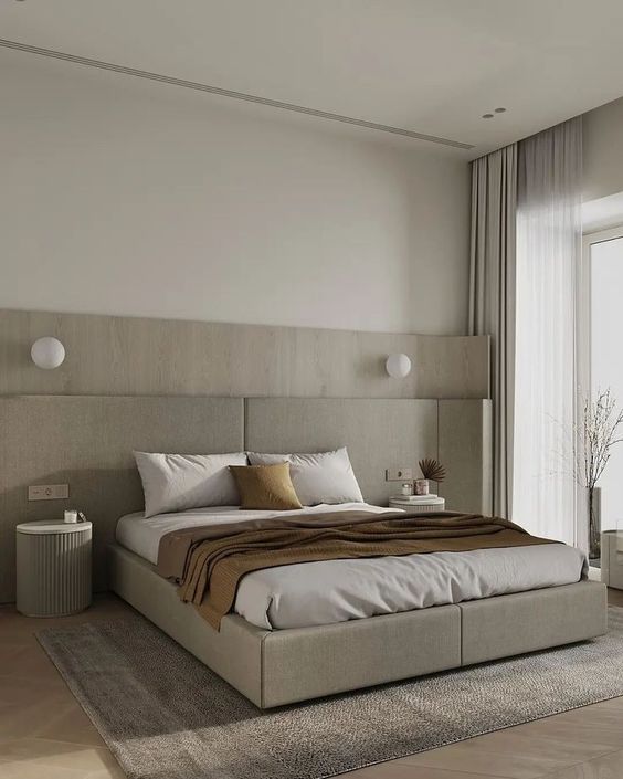 a beautiful serene bedroom done in the shades of greige and grey, with an upholstered with an extended headboard, nightstands and lights