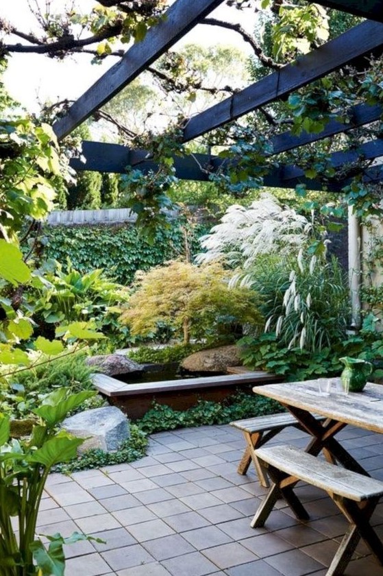 a beautiful townhouse garden with planted greenery, lush and textural herbs, a pond, tiles and a wooden dining set