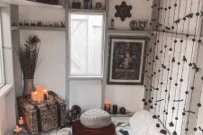 a boho black and white she shed with cushions and pillows on the floor, a tassel screen, open shelves, candles and branches