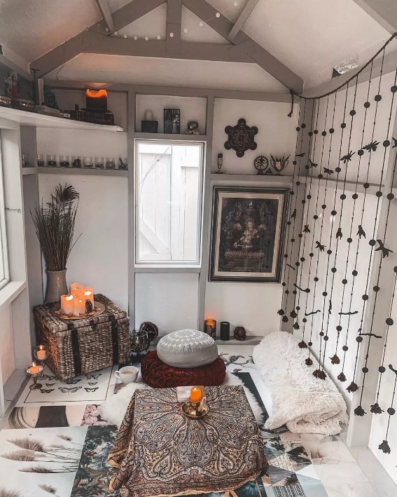 a boho black and white she shed with cushions and pillows on the floor, a tassel screen, open shelves, candles and branches