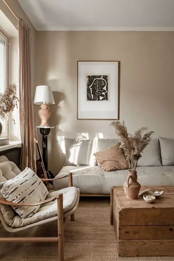 a boho-inspired greige living room with a grey sofa, a chair with a printed pillow, a wooden coffee table and an artwork