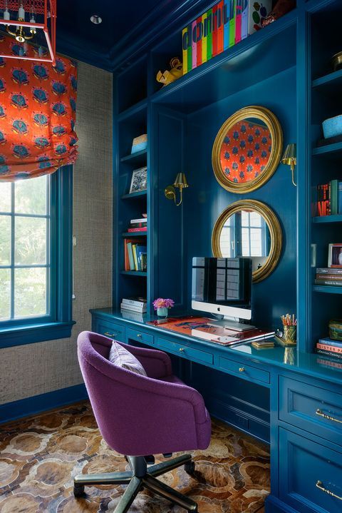 a bright home office with a blue storage unit with a built-in desk, a purple chair, an orange curtain and some colorful books