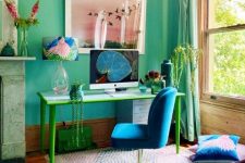 a bright home office with emerald walls, a fireplace, a green and blue desk, a blue chair, pink and blue textiles and a pink artwork