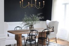 a catchy dining room with black walls and white panels, a stained table, white armchairs and black chairs, a vintage chandelier