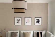 a catchy greige living room with a creamy sofa and printed pillows, a grid gallery wall, a catchy two tone pendant lamp and round side tables