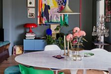 a catchy home office with grey walls and a ceiling, a white table, colorful mismatching chairs, a blue credenza and colorful artwork
